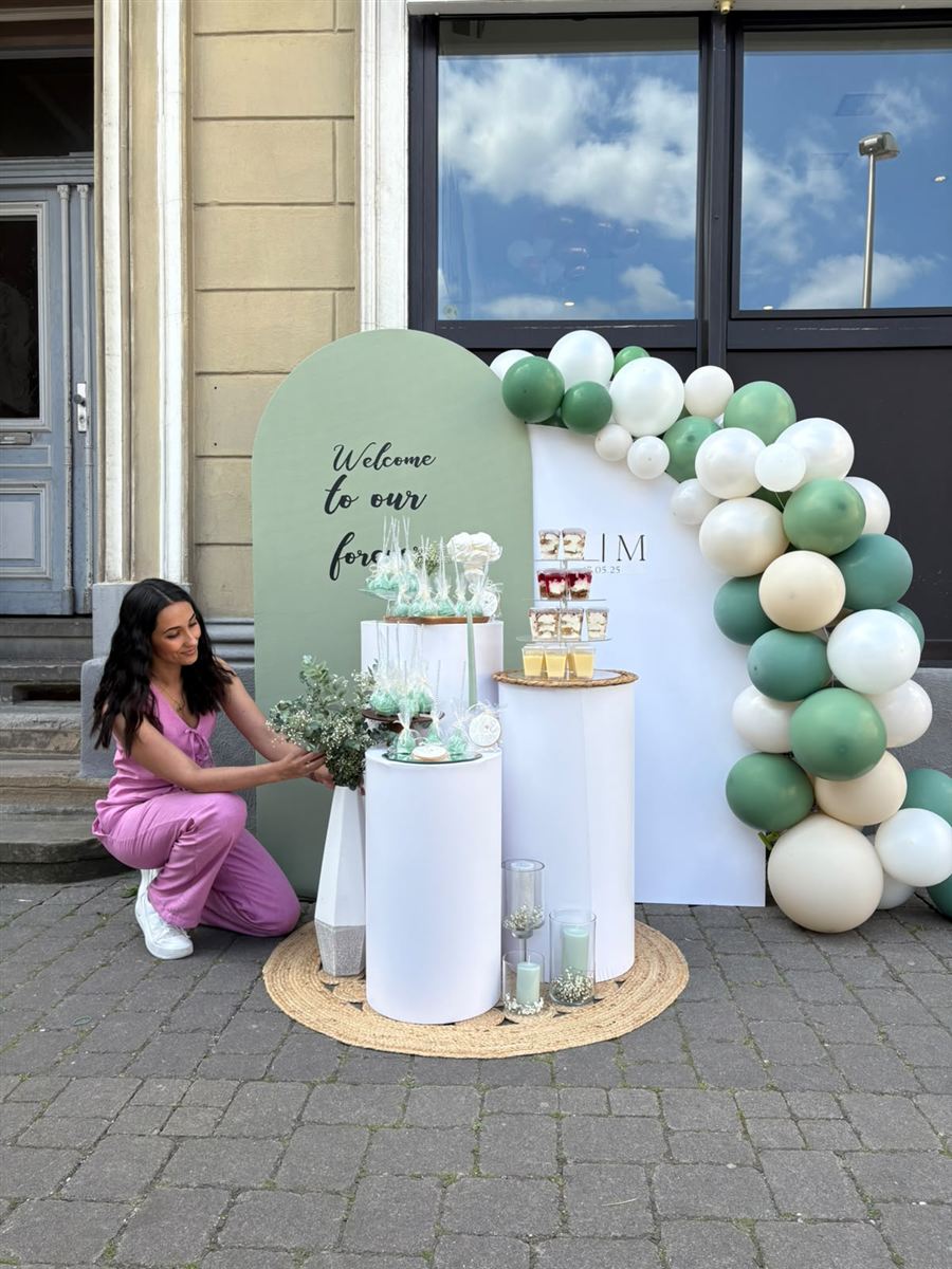 Eleni arrangiert Eukalyptuszweige an einer Hochzeitsdeko mit grün-weißer Ballongirlande vor einem Altbau