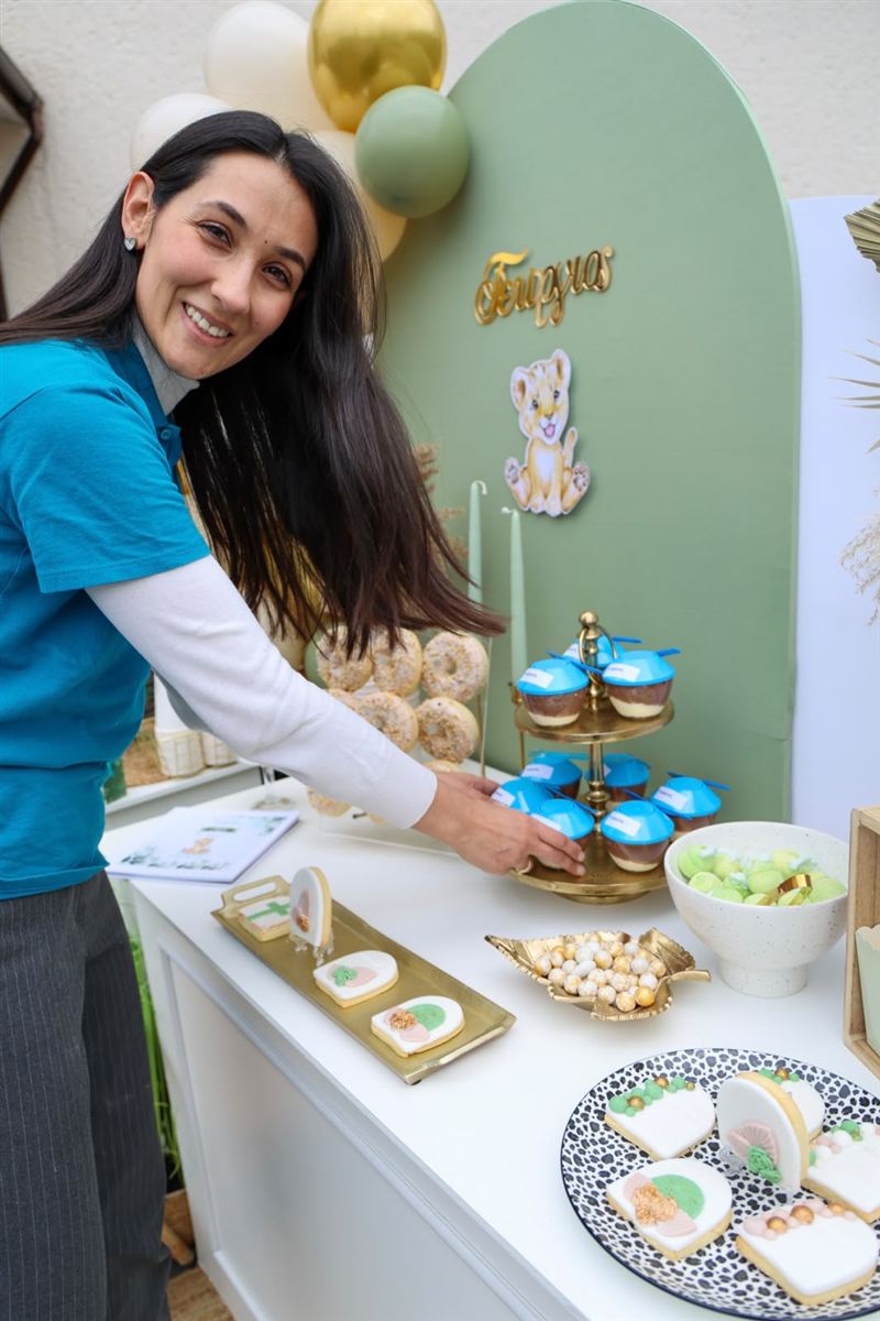 Eleni Liodis lächelt in die Kamera, während sie einen Sweet Table mit Löwen-Motto in Salbeigrün und Gold aufbaut