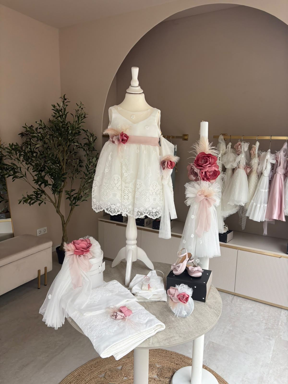 Innenraum des Design-Miracle-Ateliers: Taufkleid auf Schneiderbüste vor beigem Rundbogen, daneben Kleidchen in Weiß und Rosa